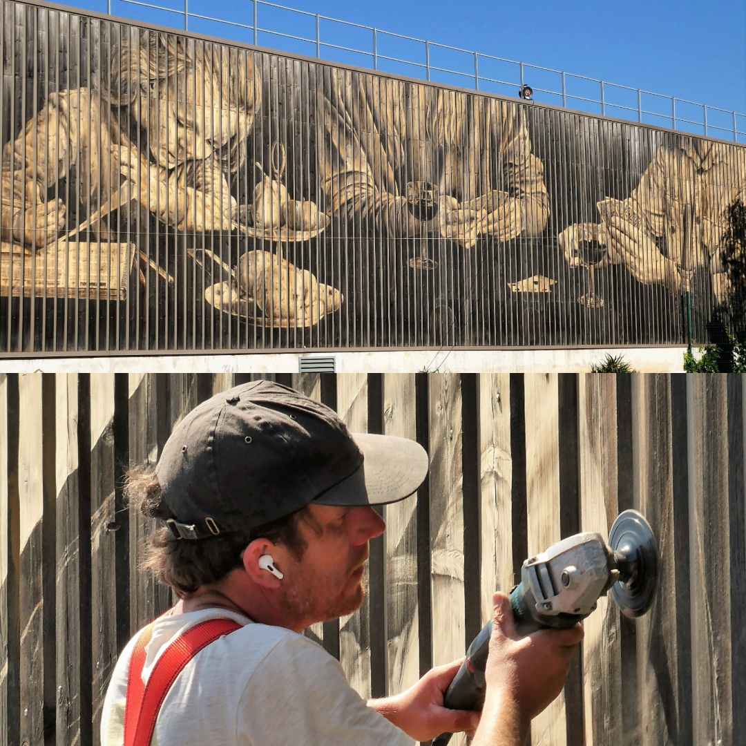 Street artist LPVDA draws with a grinder on a wooden wall blackened by time. The clear parts are sanded by the grinder